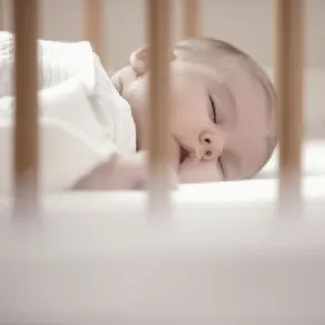 neonato che dorme nel lelttino con sbarre in legno