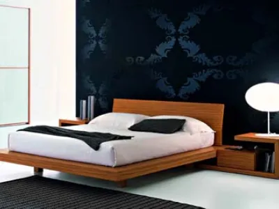letto matrimoniale con struttura in legno e biancheria bianca e cuscino nero, comodino integrato e parete con carta da parati in broccato blu scuro
