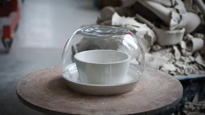 ciotola e sotto piatto in ceramica bianca con campana in vetro trasparente su tavolino rotondo in legno