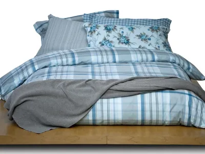 letto matrimoniale con copripiumino scozzese sui toni blu e tortora, coperta tortora e cuscini a rose blu