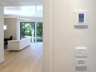 dettaglio di consolle di controllo su parete, vista di zona living con divano bianco e parete finestrata