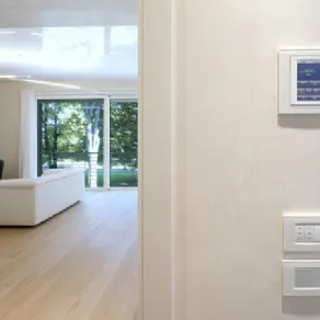 dettaglio di consolle di controllo su parete, vista di zona living con divano bianco e parete finestrata