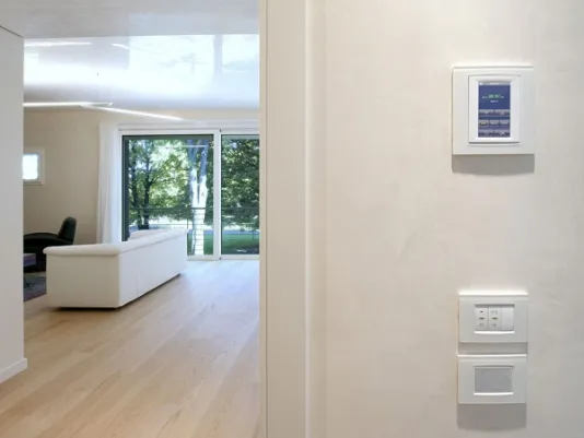 dettaglio di consolle di controllo su parete, vista di zona living con divano bianco e parete finestrata