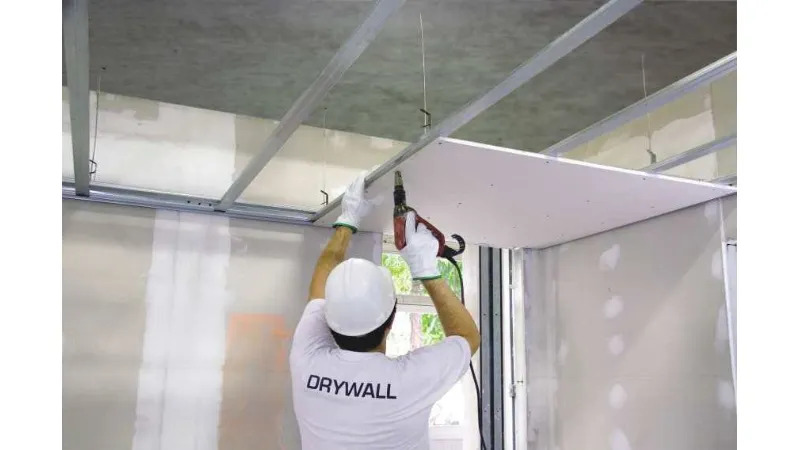 In questa foto è ritratto un operaio che fissa ai profili metallici un pannello di cartongesso: probabilmente, si tratta della realizzazione di un controsoffitto