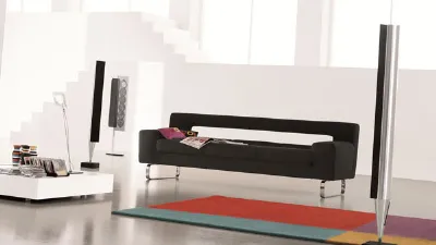 divano a tre posti nero con gambe in alluminio inserito in spazio living bianco con tappeto geometrico multicolore e casse verticali