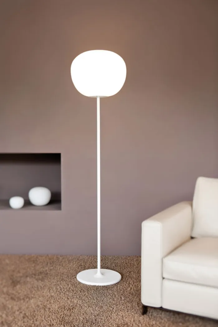 lampada da terra bianca con stelo verticale e paralume sferico, tappeto color naturale e poltrona bianca