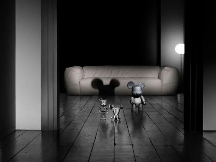tre vynil toys a forma di topo grigi e argentati, pavimento in legno grezzo e divano panna sullo sfondo