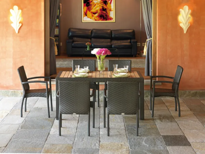 tavolo con piano in legno e profili e gambe in rattan antracite, sei sedie da esterno in rattan antracite, piastrelle in pietra e muro arancio
