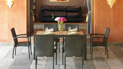 tavolo con piano in legno e profili e gambe in rattan antracite, sei sedie da esterno in rattan antracite, piastrelle in pietra e muro arancio