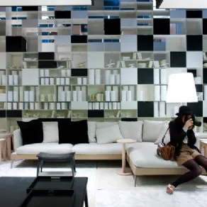 spazio espositivo con mobili zona living con libreria a parete bianca e nera, divano con chaise-longue in legno chiaro e tessili in ecrù e nero, due visitatori