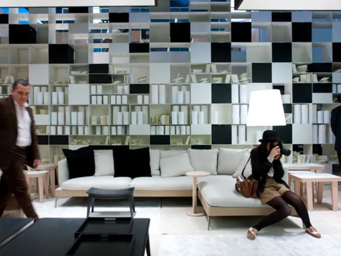 spazio espositivo con mobili zona living con libreria a parete bianca e nera, divano con chaise-longue in legno chiaro e tessili in ecrù e nero, due visitatori