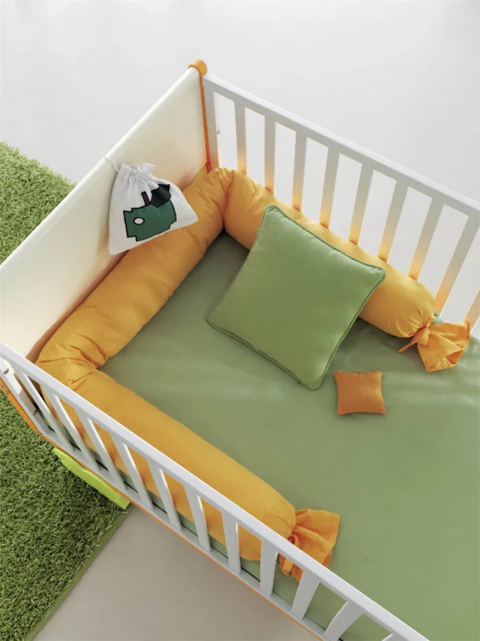 dettaglio interno lettino in legno bianco con tessili verdi e gialli, tappeto effetto erba