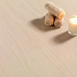 tre asciugamani arrotolati con candela su superficie in simil Travertino