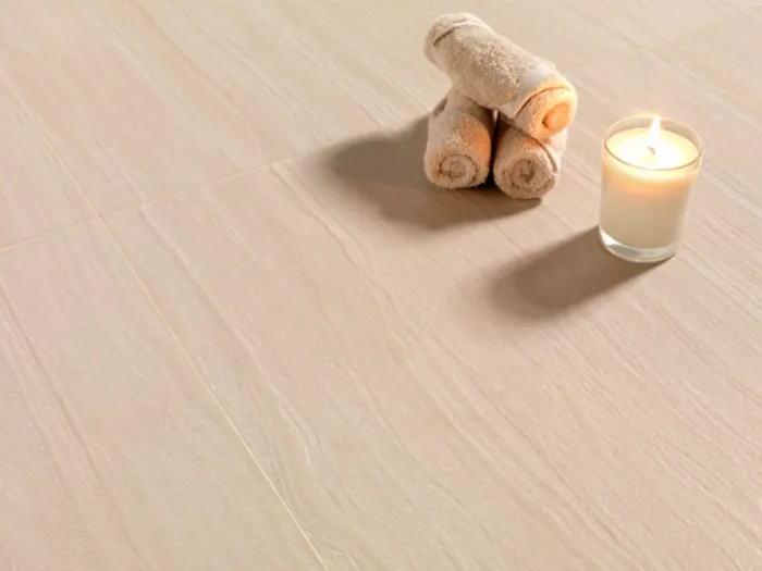 tre asciugamani arrotolati con candela su superficie in simil Travertino