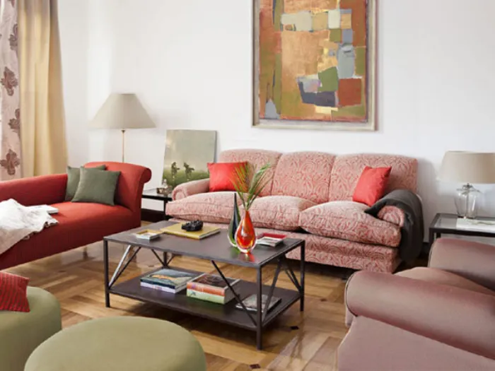 salotto con divani, cuscini e pouf nei toni del verde oliva e rosso mattone, tavolino marrone scuro e quadri astratti dai colori coordinati