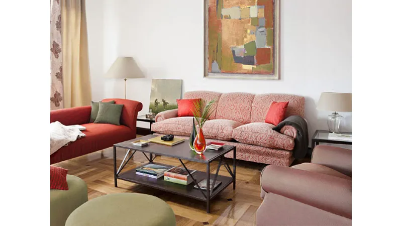 salotto con divani, cuscini e pouf nei toni del verde oliva e rosso mattone, tavolino marrone scuro e quadri astratti dai colori coordinati