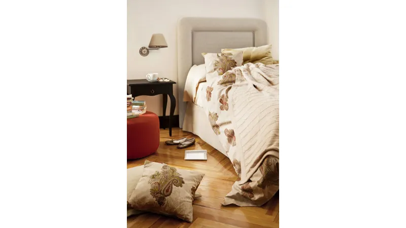 letto matrimoniale con tessili e cuscini color panna con fantasie floreali jacquard, pouf rosso