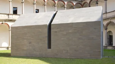 casa in pietra grigia con apertura verticale nel centro all'interno di chiostro con prato