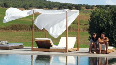 Coppia seduta a bordo piscina con baldacchino e lettini da esterni