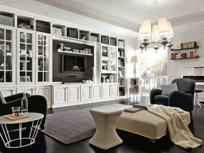 spazio living con scaffalatura bianca, vetrine e spazio tv, poltrone nere, puof e lampadario con paralumi