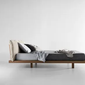 vista laterale di letto matrimoniale con struttura in legno, testiera di cuscini color panna e biancheria nei toni del grigio 