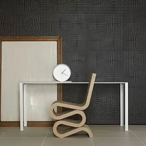seduta design in gres porcellanato vista di profilo, cornice in legno appoggiata alla parete e tavolo bianco con orologio