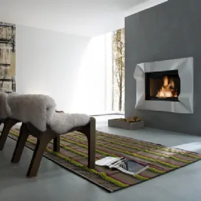 caminetto su parete grigia con cornice geometrica bianca, due poltrone in legno con rivestimento in pelo bianco, tappeto a fantasia a righe verde mela e pink