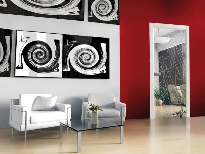 zona living con quadri astratti bianchi e neri su pareti rosse, tavolino in vetro trasparente, due poltrone bianche, porta trasparente con grafiche bianche