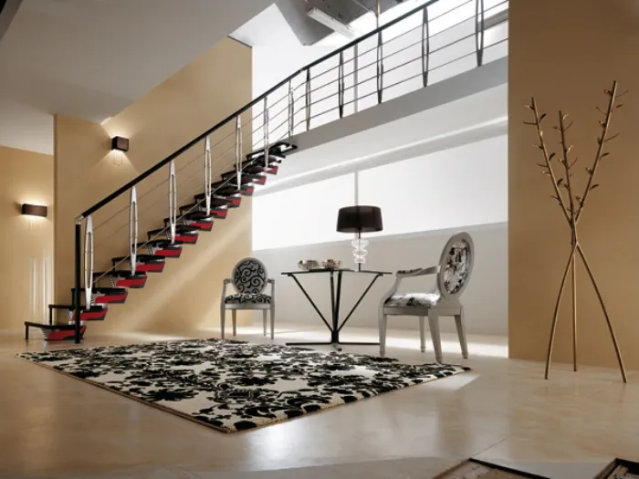 veduta angolare di zona living con scala con gradini neri e dettagli rossi, tappeto bianco con disegni neri, due sedie luigi XVI con stesso rivestimento