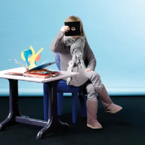 bambina seduta su sedia blu, tavolino con libro pop-up