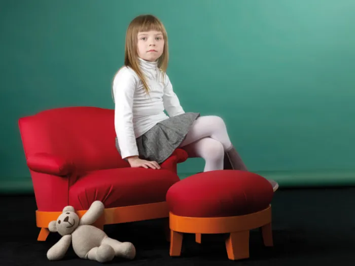 bambina seduta seu mini poltroncina arancio e rossa, pouf abbinato e orsetto peluche