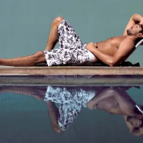 uomo in boxer con grafiche nere su sfondo bianco su bordo piscina su sedia Beachbuddy