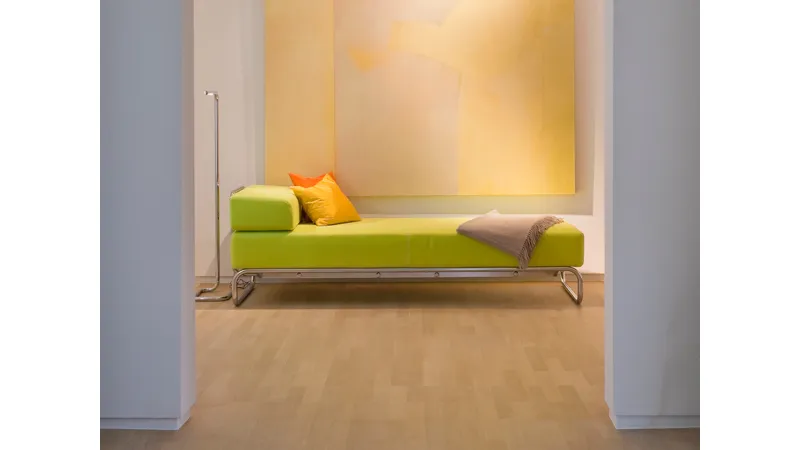 divano chaise-longue verde mela, cuscini giallo e arancio, coperta ecrù, quadro astratto giallo