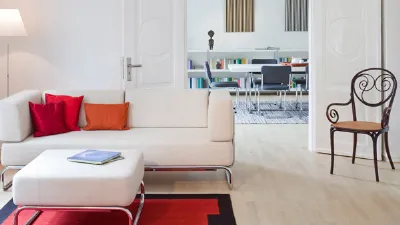zona living con divano e pouf bianco con gambe in acciaio, cuscini e tappeto rossi, sedia in legno nero e seduta in legno naturale