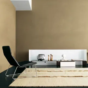 spazio living con parete beige, poltrona design nera, tappeto naturale e tavolini con spalliera bianca