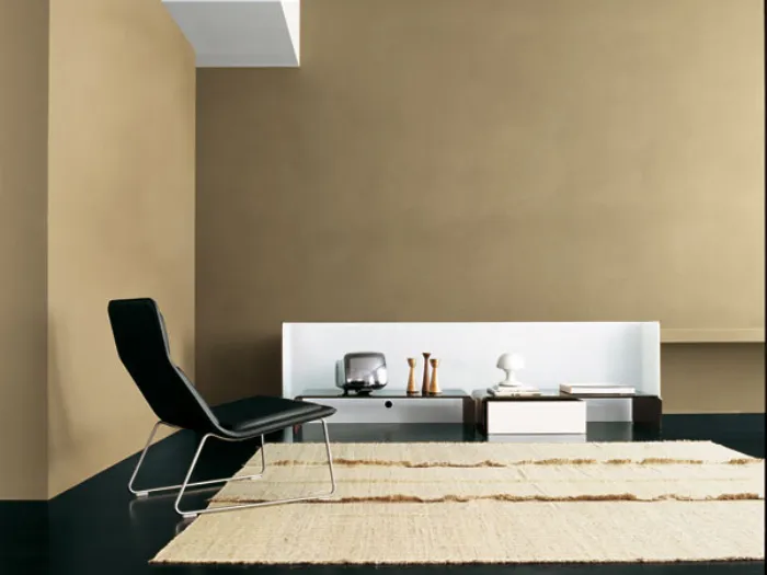 spazio living con parete beige, poltrona design nera, tappeto naturale e tavolini con spalliera bianca