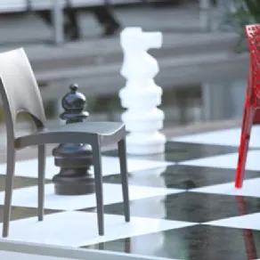 sedia grigia su pavimento a scacchiera, sedia rossa sullo sfondo e due scacchi