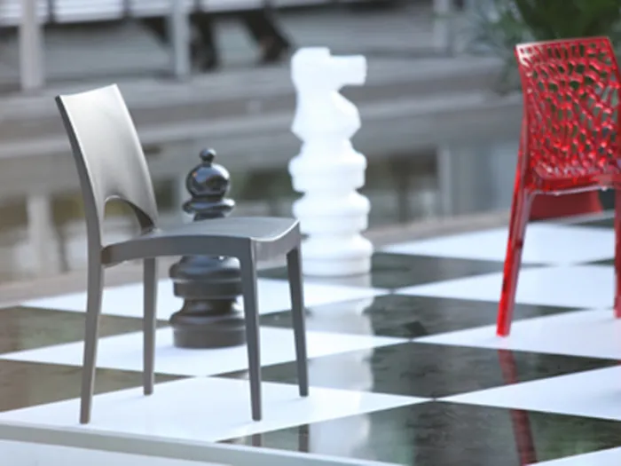 sedia grigia su pavimento a scacchiera, sedia rossa sullo sfondo e due scacchi