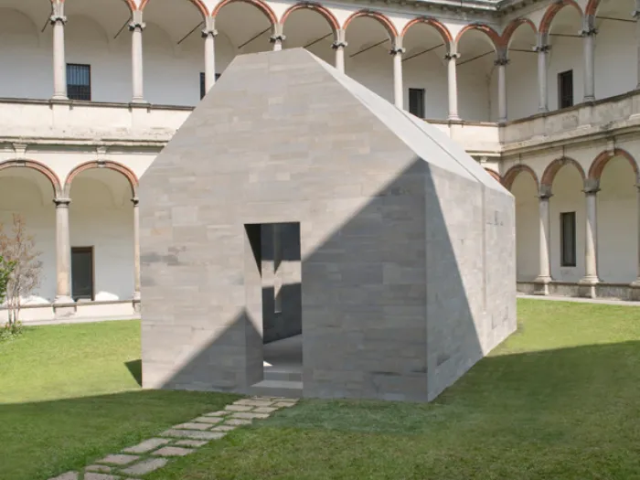 casa in pietra grigia con apertura verticale nel centro all'interno di chiostro con prato